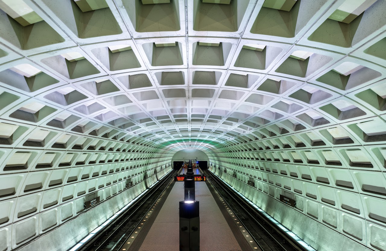 Interior of Metro station with vaulted ceiling, platform, and two train tracks.